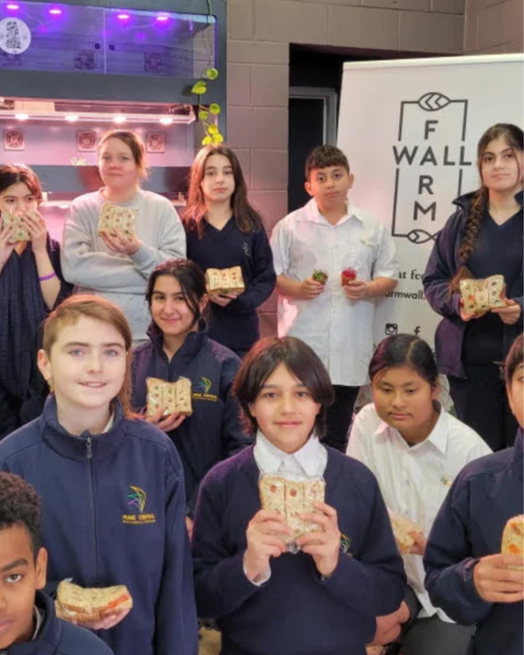 Students holding food in front of a Farmwall growing unit